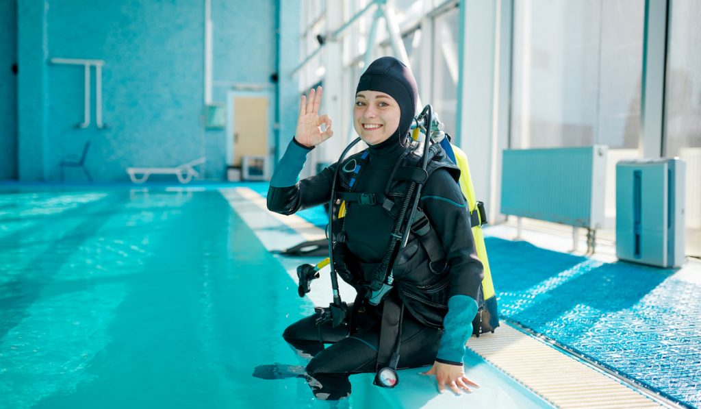 Female diver in scuba suit sitting at the poolside ready to practice diving 