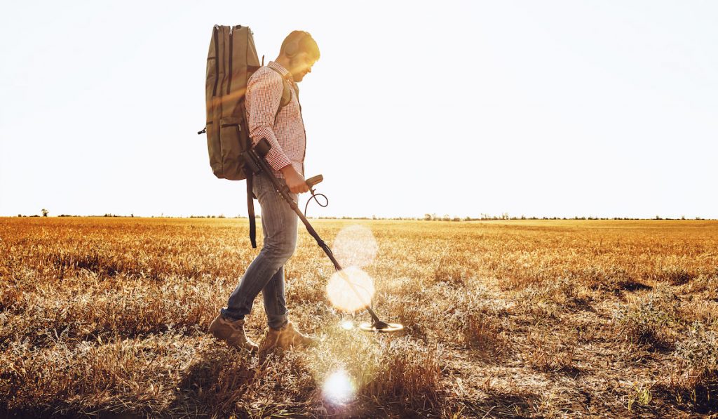 Man with metal detector equipment searching for metal goods in the field