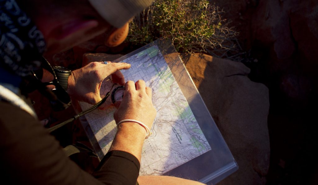 Overhead View Of Man Using Navigational Compass On Map While Sitting On Field