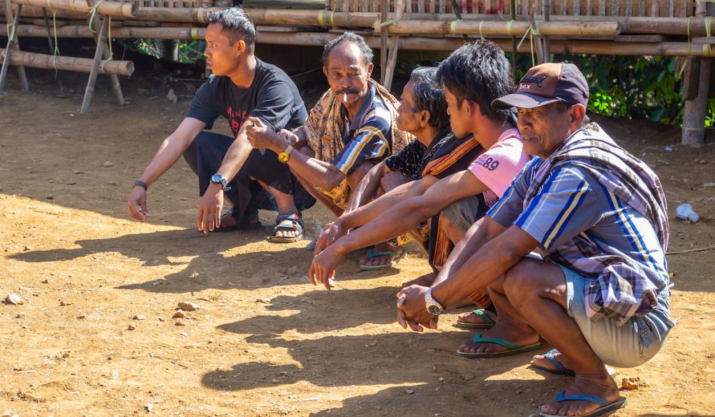 group of local residence sitting on haunches and talking in old village