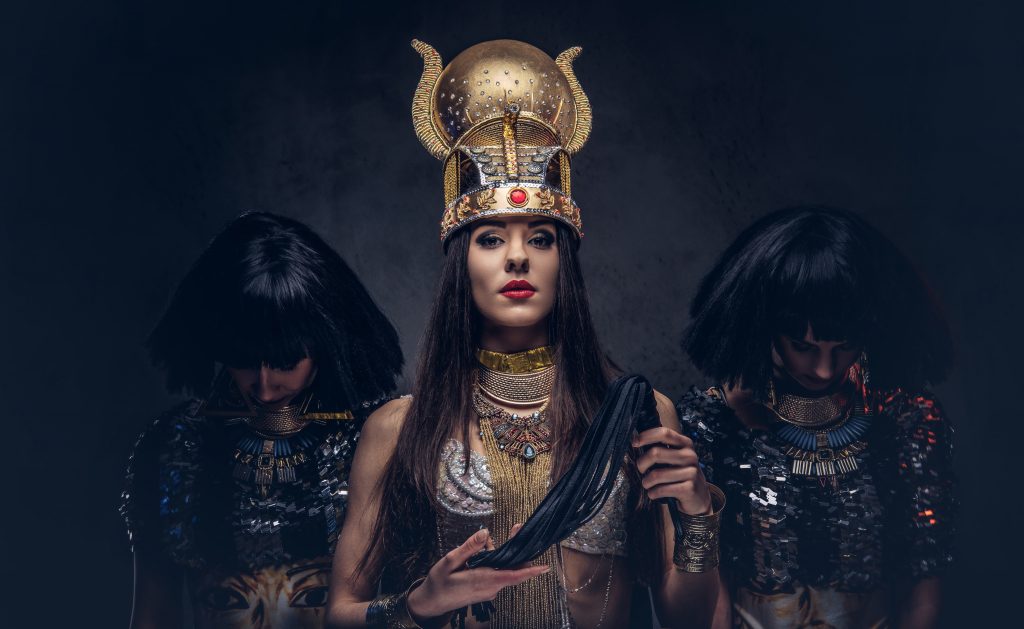 Portrait of haughty Egyptian queen in an ancient pharaoh costume with two concubines