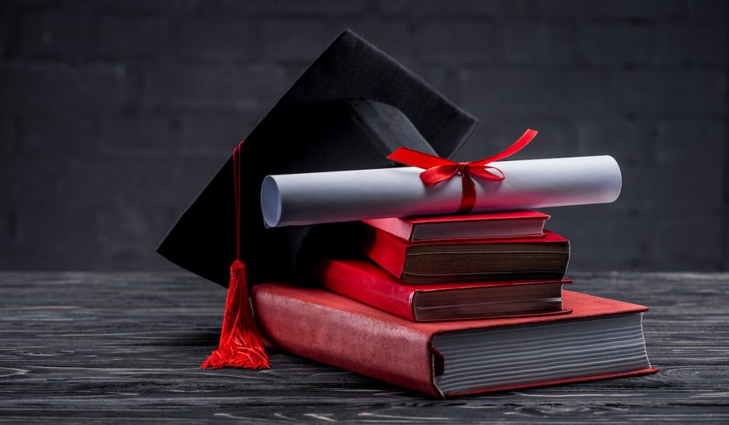 Stack of books with diploma and graduation hat on table