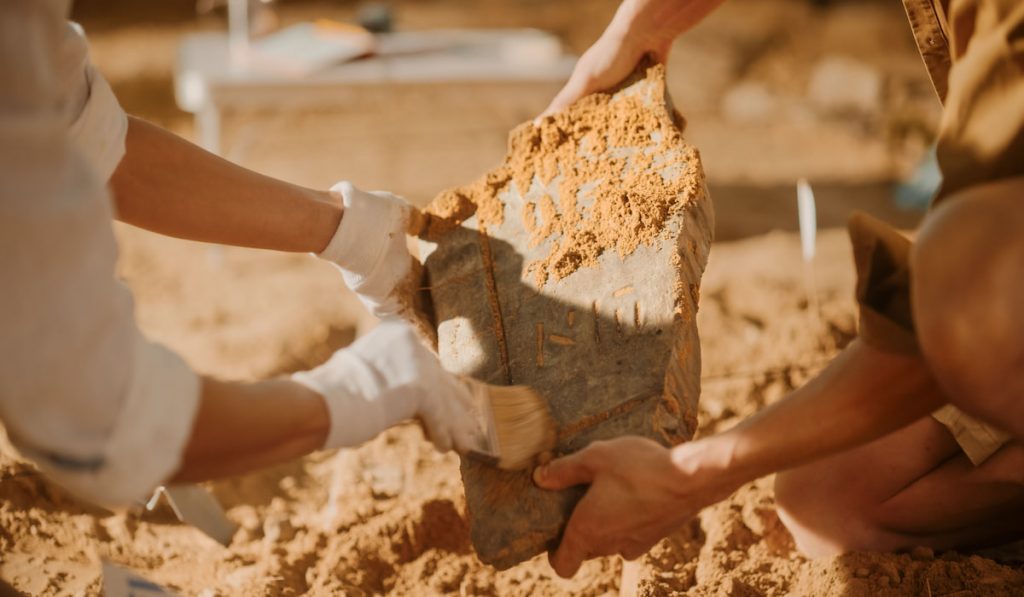 Two Great Archeologists Work on Excavation Site, Carefully Cleaning, Holding Newly Discovered Ancient Civilization Cultural Artifact 